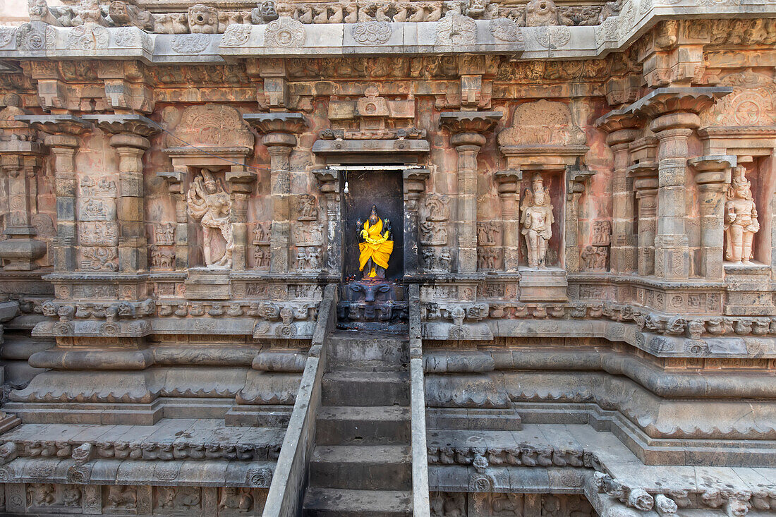 Treppe, die zu einer Nische mit einer in leuchtend gelbe Seide gehüllten Hindu-Gottheit in einer Steinmauer des Airavatesvara-Tempels aus der dravidischen Chola-Zeit führt; Darasuram, Tamil Nadu, Indien