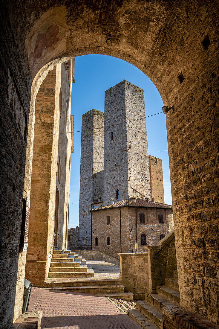 Blick durch einen Bogengang auf die mittelalterlichen Türme im historischen Zentrum von San Gimignano; San Gimignano, Toskana, Italien