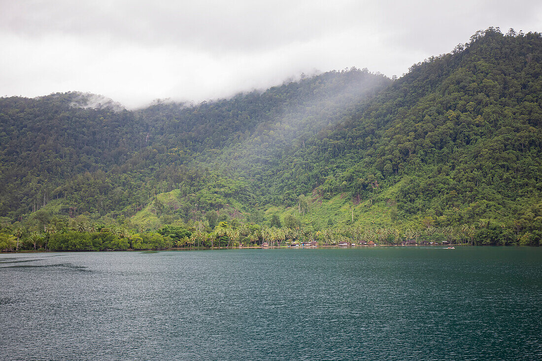 Dampf, der über den Dschungelhügeln mit dem Dorf Siboma entlang der Küstenlinie der Insel Lababia im Huon-Golf aufsteigt; Siboma, Provinz Morobe, Papua-Neuguinea