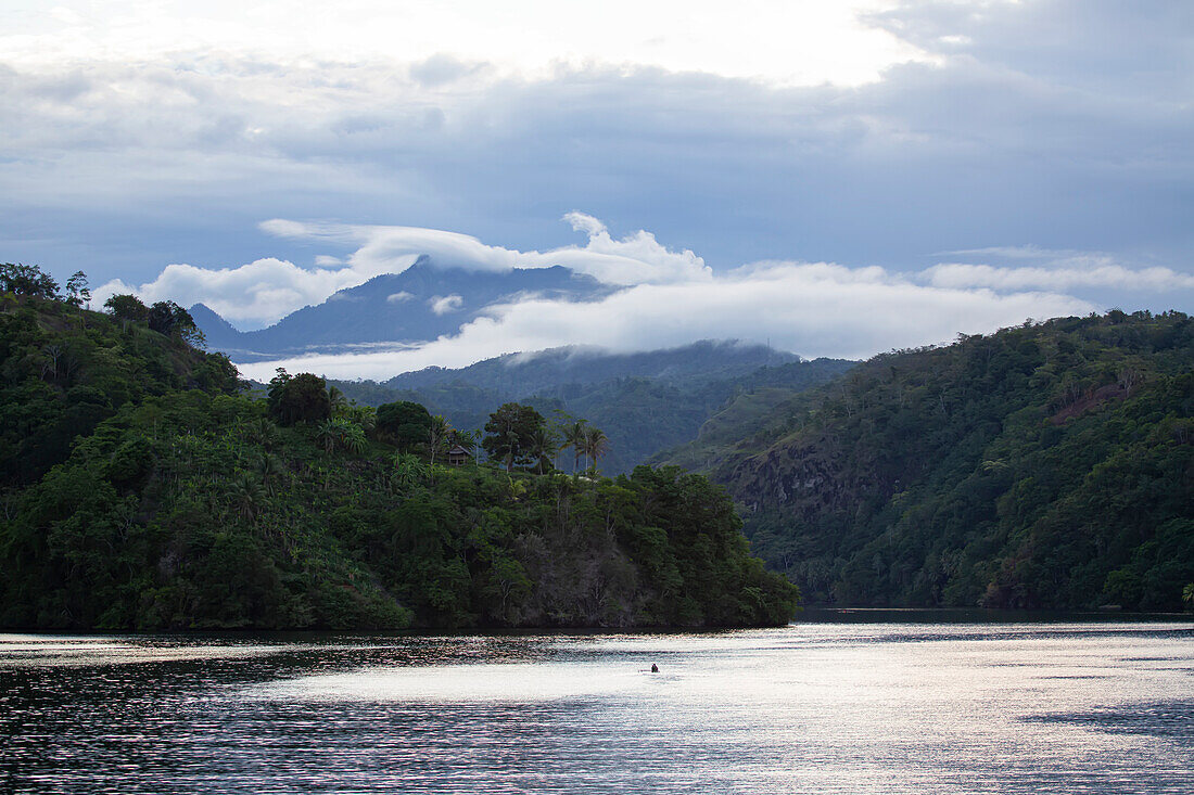 Clouds swirling around mountains of the Tufi tropical sea fjord with outrigger canoe on the Cape Nelson peninsula; Tufi, Oro Province, Papua New Guinea