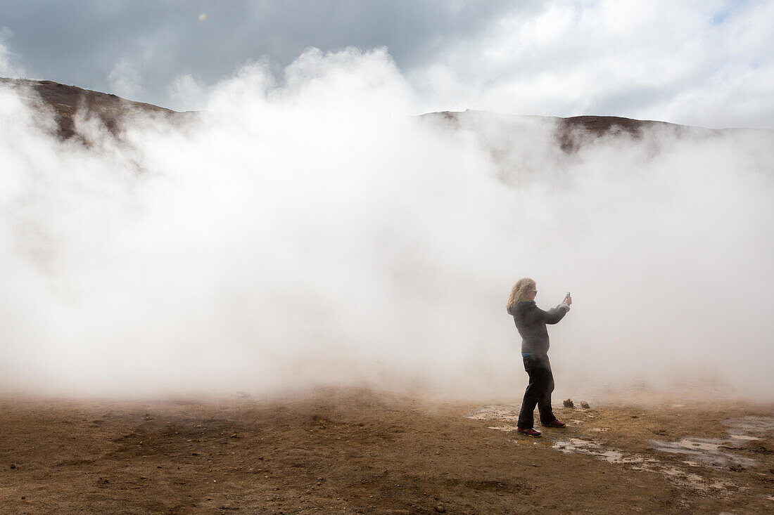 Eine Frau fotografiert inmitten der dampfenden Schlammtöpfe im geothermischen Gebiet in der Nähe des Myvatn-Sees; Island