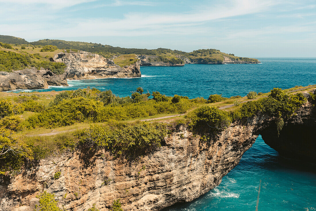 Grün bewachsener Meeresbogen, Felsformation entlang der felsigen Küste der Nusa Inseln; Nusa Penida, Provinz Bali, Indonesien