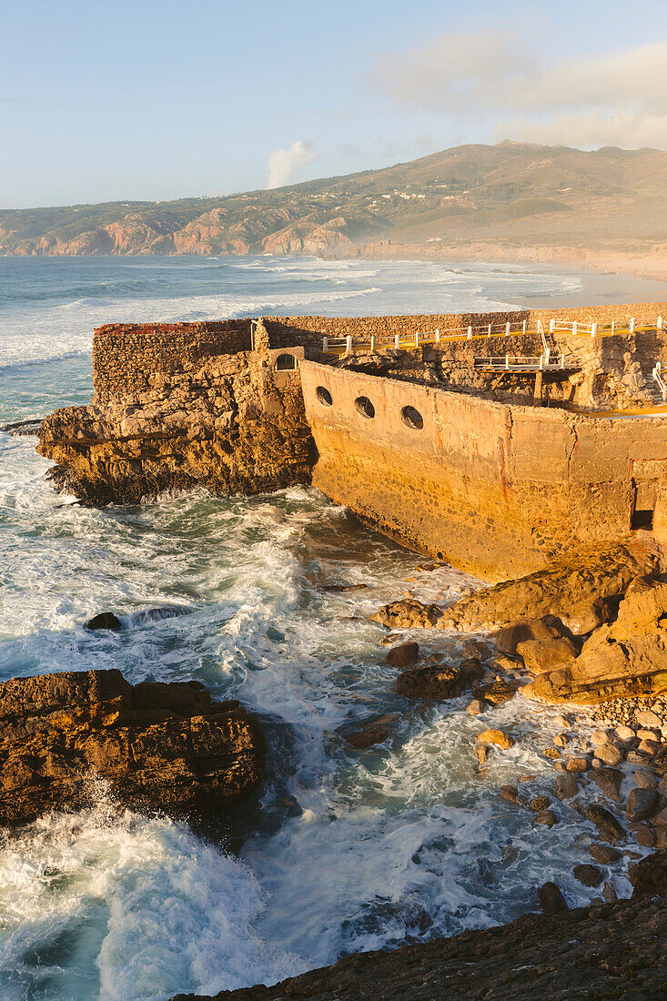 Atlantic Ocean waves along the shores of the Praia do Guincho near Cascais with the Estalagem Muchaox hotel's outdoor swimming pool built within the stone wall ruins of an old fort; Praia do Guincho, Cascais, Lison, Portugal