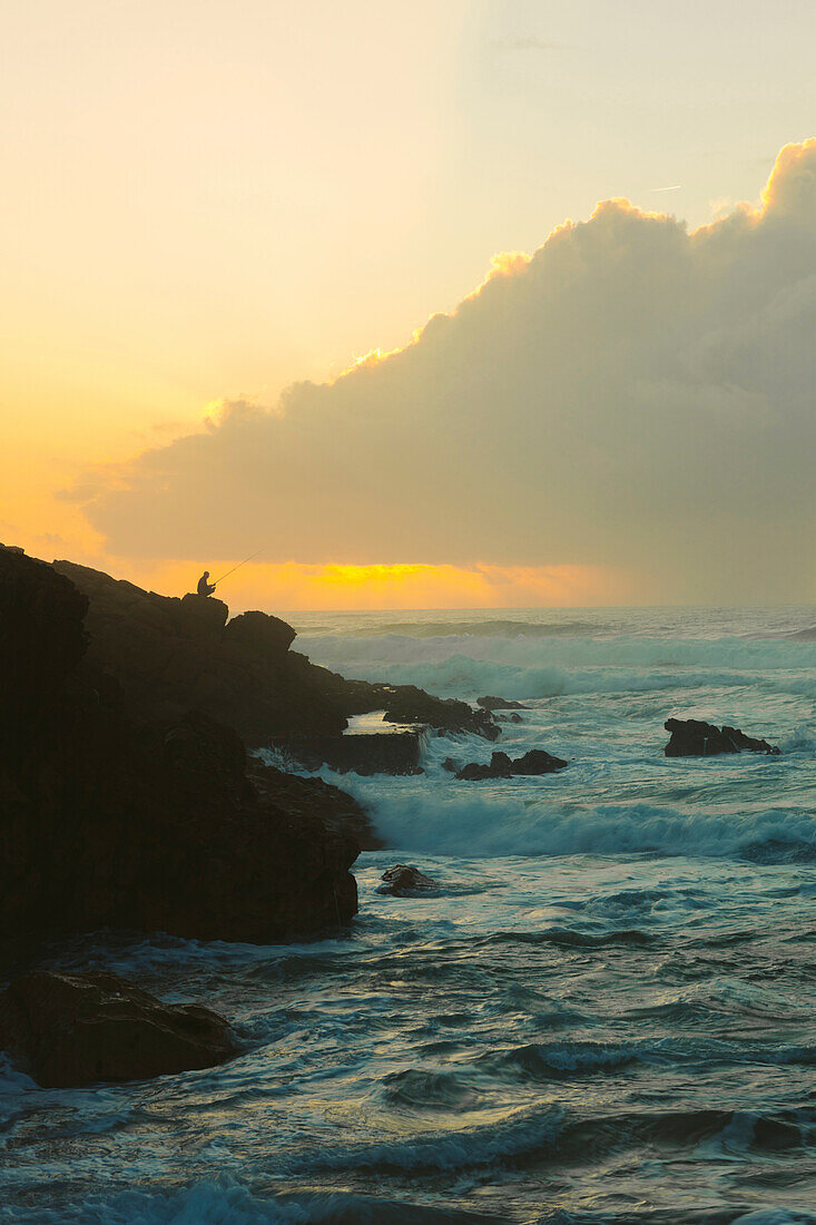 Silhouette of man surf fishing along a rugged coastline at sunset; Praia do Guincho, Cascais, Portugal