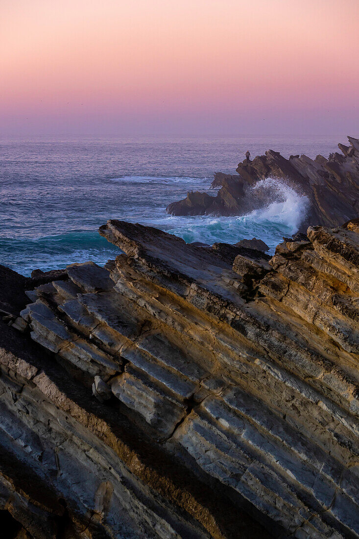 Pink glowing sunset sky over the Atlantic Ocean and the rugged rocks lining the coastline at Praia Baleal; Peniche, Oeste, Portugal