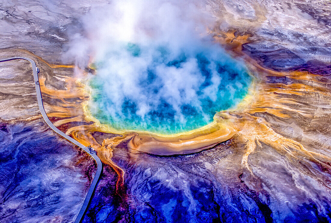 Grand Prismatic Spring ist eines der größten und schönsten Beispiele für eine häufige hydrothermale Erscheinung im Yellowstone National Park und eine der größten heißen Quellen in den Vereinigten Staaten. Das tiefe Blau in der Mitte ist das klare, überhitzte Wasser, das aus der unterirdischen Wärmequelle nach oben fließt, und wenn das Wasser an den Rändern des Beckens und auf den Sinterterrassen abkühlt, erzeugen Bakterien und Algen den Regenbogen der Farben. Diese heiße Quelle wurde in Osborne Russells Journal of a Trapper ausdrücklich unter dem Namen Boiling Lake erwähnt, der offenbar von Pe