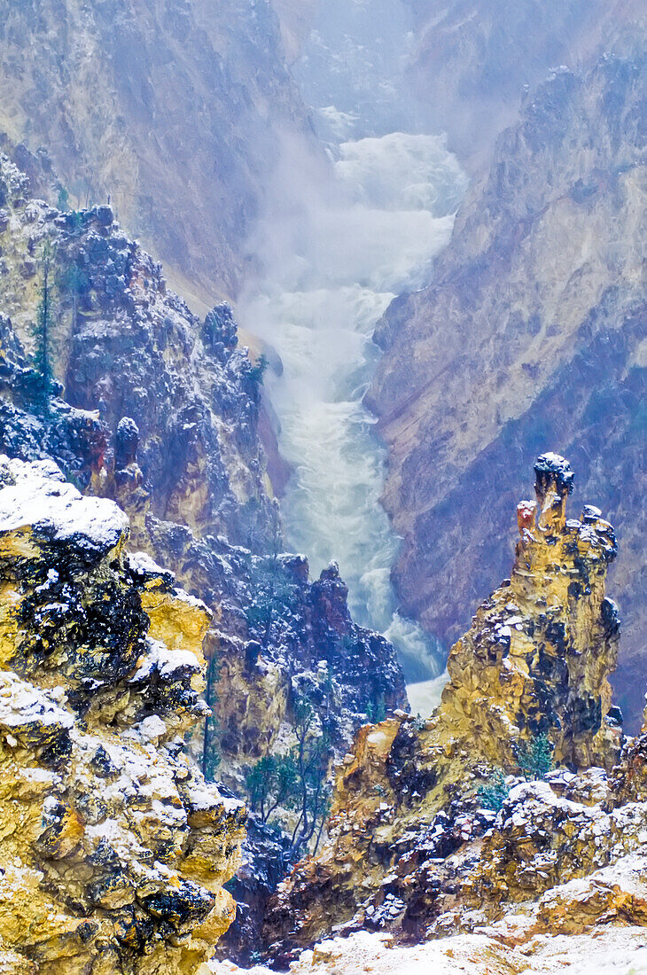 Nebel über dem rauschenden Wasser des Yellowstone River im Grand Canyon of the Yellowstone mit den farbenfrohen, zerklüfteten Rhyolith-Klippen, die von einem Winterschneefall bedeckt sind; Yellowstone National Park, Wyoming, Vereinigte Staaten von Amerika