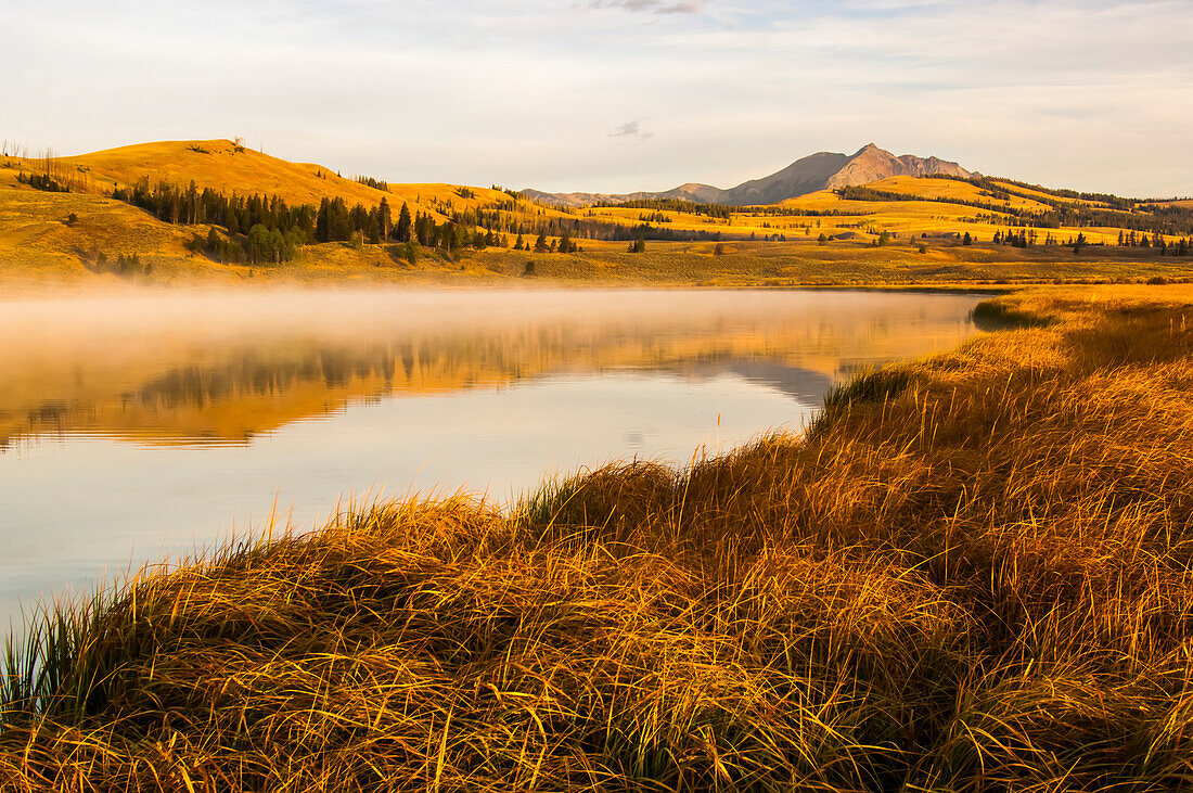 Golden sunlight over Electric Peak and the Gallatin Range reflected in Swan Lake of the Swan Lake Flats in autumn, Yellowstone National Park; Wyoming, United States of America