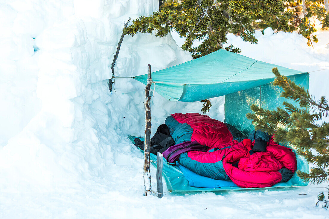 Wintercamping am Big Game Ridge mit Schlafsack unter einem behelfsmäßigen Unterstand mit einer an Bäumen befestigten Nylonmarkise im Hinterland des Yellowstone National Park; Wyoming, Vereinigte Staaten von Amerika