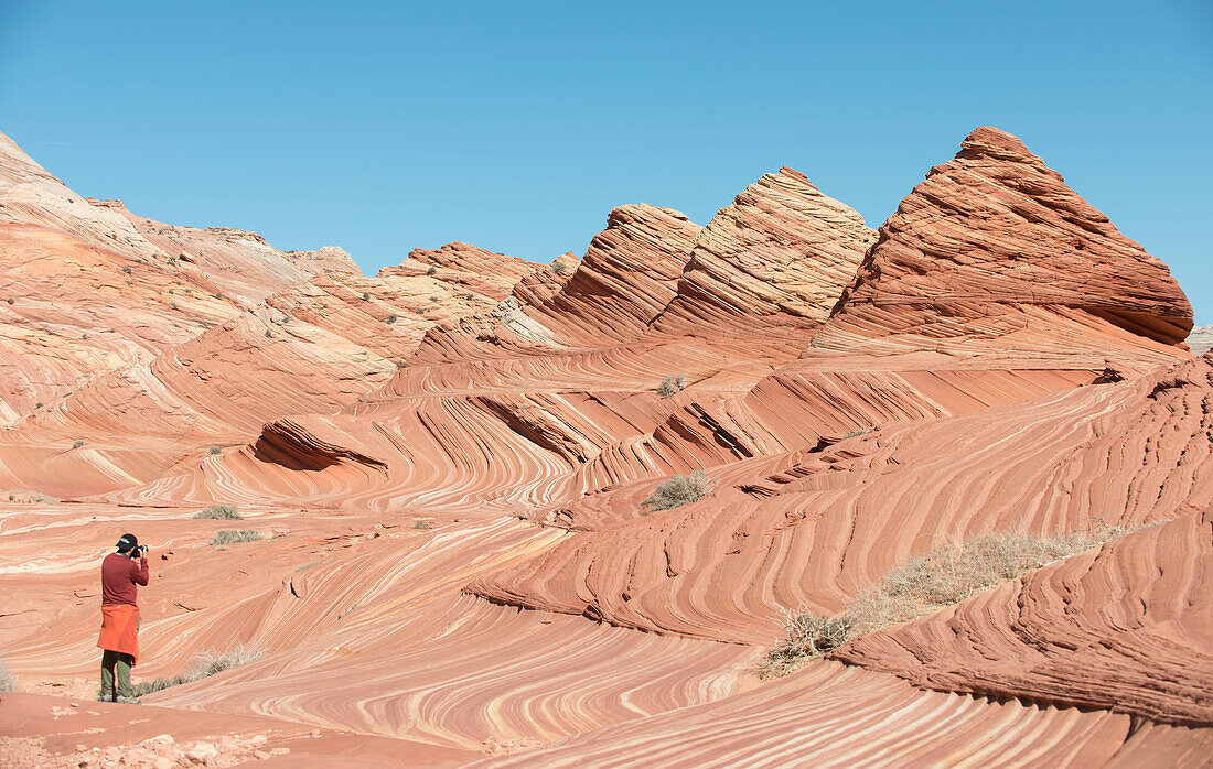 A man takes a picture of pyramid shaped sandstone formations in Coyote Buttes North.