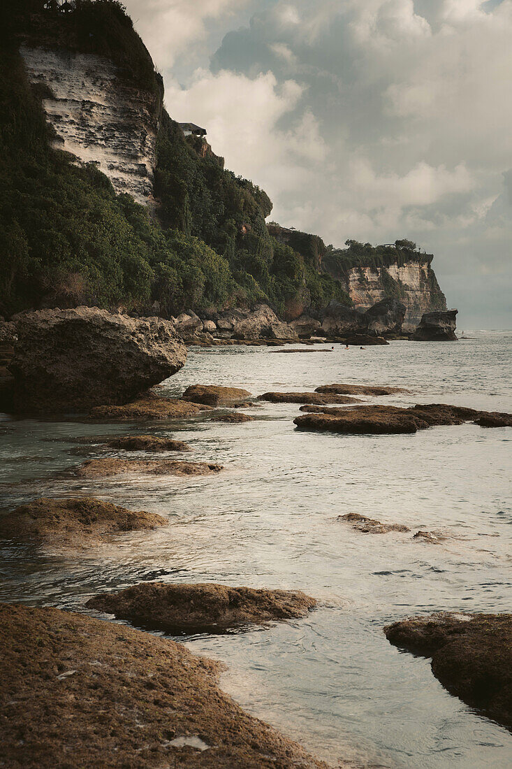 Rugged cliffs and foliage along a coastline with cloud formations in the sky, Diamond Beach; Nusa Penida, Bali, Indonesia