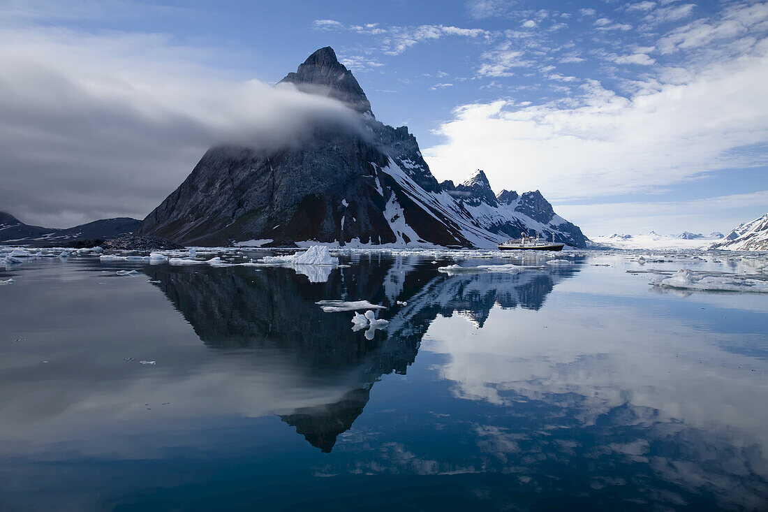 Jagged coastal peaks casting reflections in cold Arctic waters.