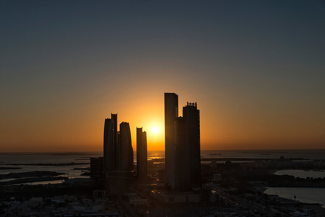 Blick auf die Hochhaussilhouetten entlang der Küste des Persischen Golfs bei Sonnenuntergang; Abu Dhabi, Vereinigte Arabische Emirate