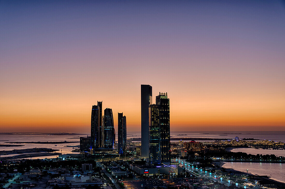 View of the silhouetted highrise towers along the Persian Gulf coast illuminated with lights at sunset; Abu Dhabi, United Arab Emirates