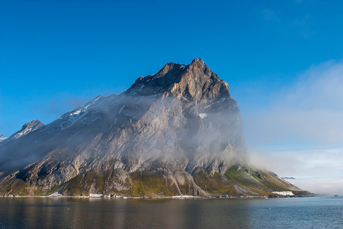 Clouds and mist clinging to jagged mountains with fjord below.