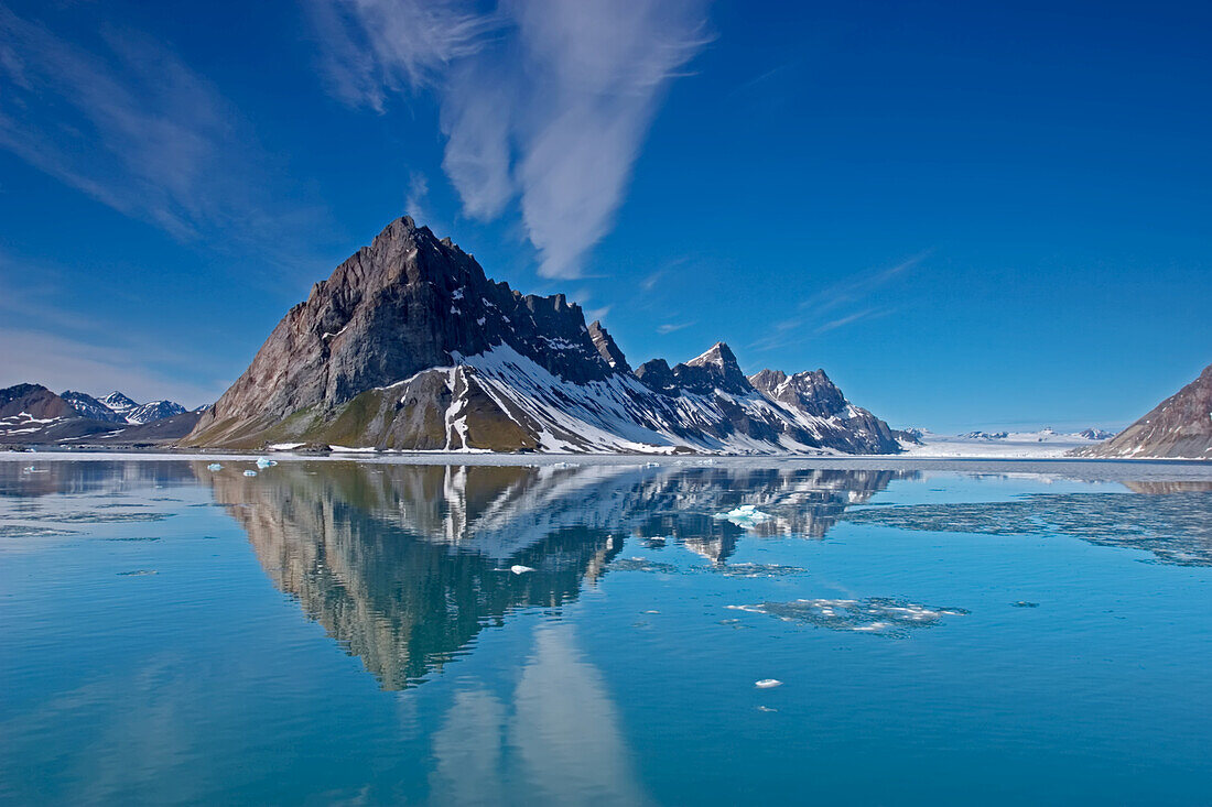 A jagged mountains casting a reflection into the melting fjord below.