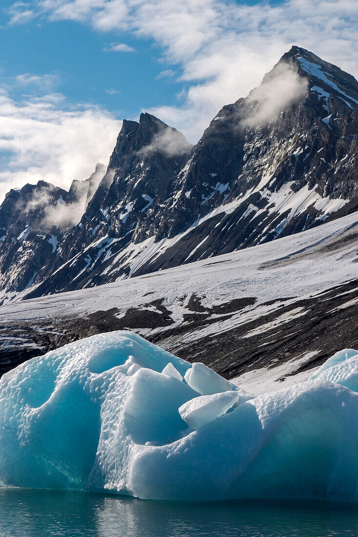 Blue ice, clouds, jagged mountains in an Arctic environment.