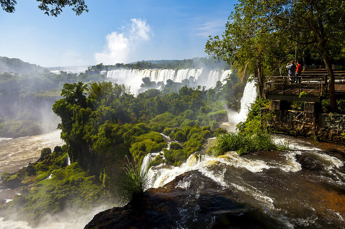 Tourists stand on a viewing platform overlooking Iguazu Falls.