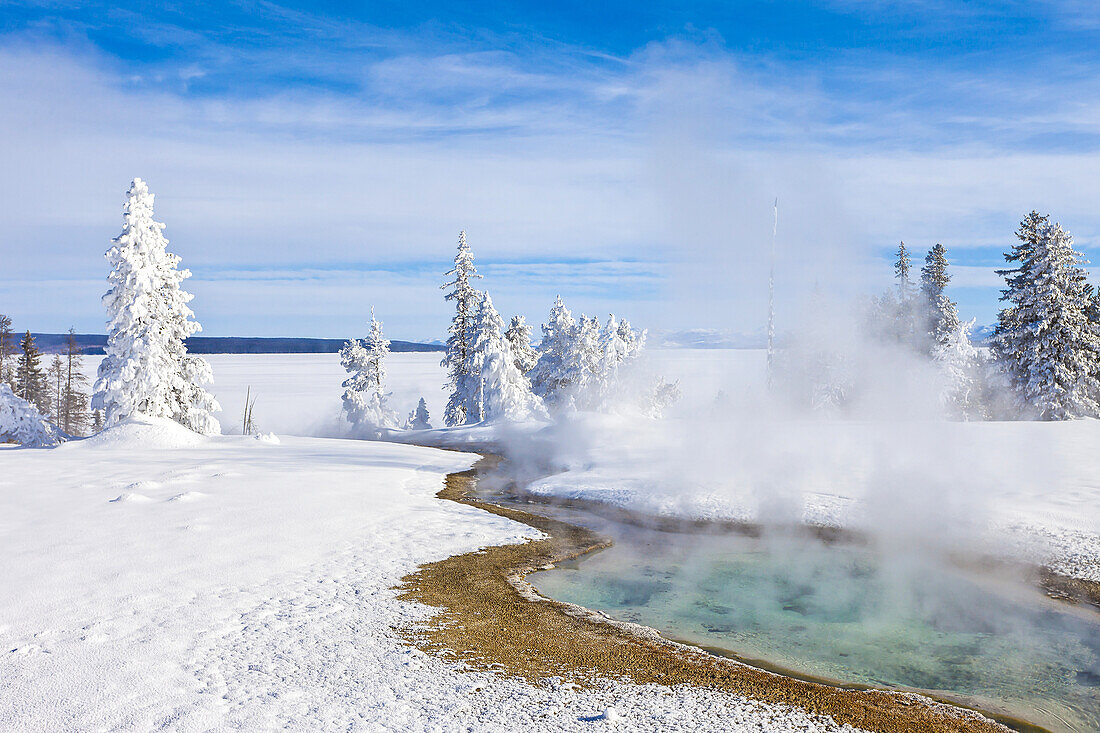 Dampf steigt aus einer heißen Quelle in einer verschneiten Landschaft auf.