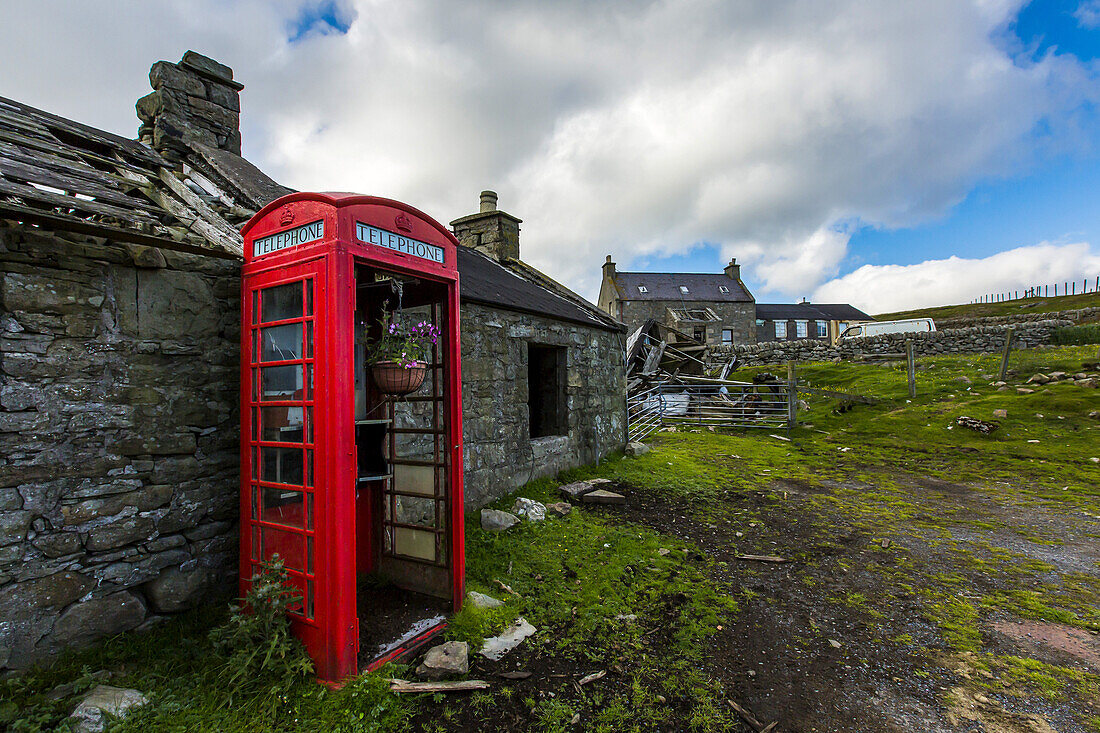 A bright red phone booth contrasts against an old stone building.