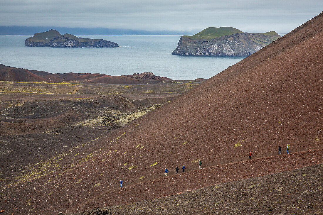 A group of hikers travel along a path up Eldfell Volcano.