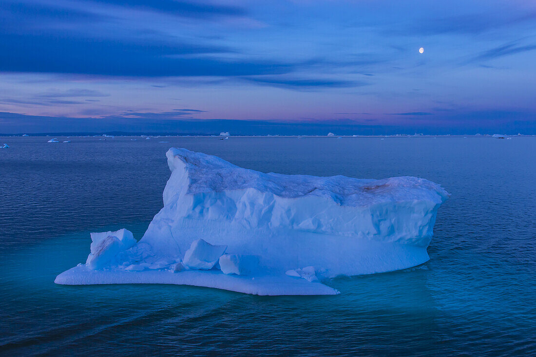 A large iceberg floats in Scorsby Sound at twilight.