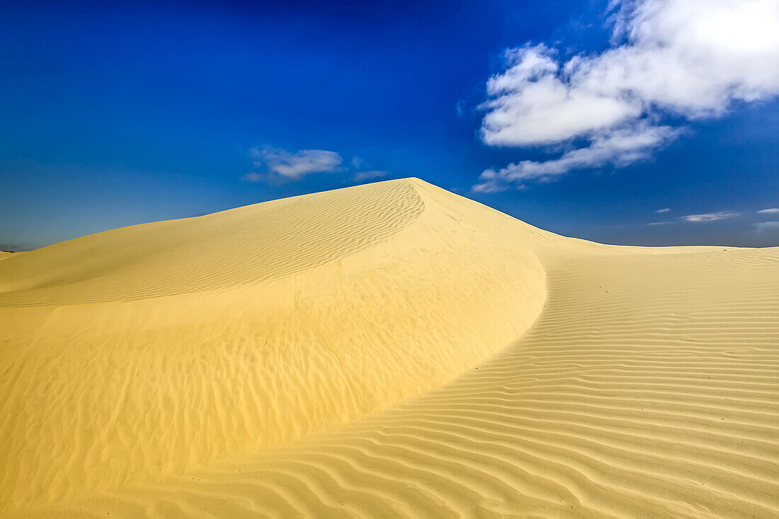 A sand dune with clouds and wind ripples.