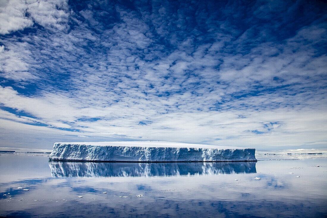 Tabular iceberg reflected in still water.