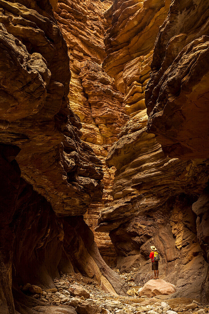 Wanderer in einem Slot Canyon, der Sandsteinschichten und Erosion beobachtet.