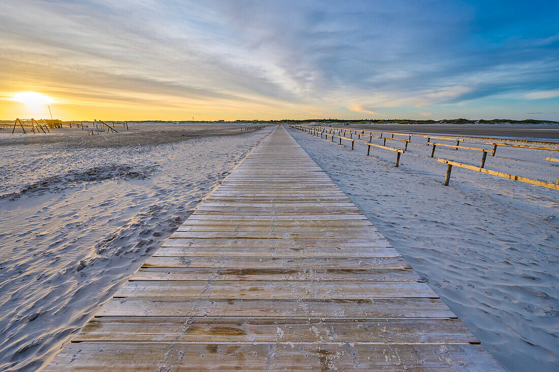 Sandstrand mit Holzplankenweg und hölzernem Fahrradgeländer bei Sonnenaufgang an der Nordsee in einem Seebad in Nordfriesland; Sankt Peter-Ording, Schleswig-Holstein, Deutschland