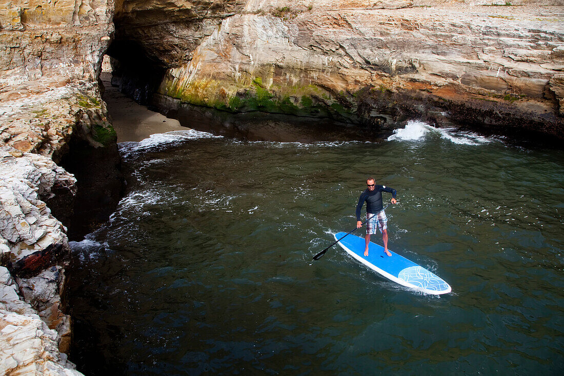 Ein Stand Up Paddleboarder an der rauen Küste nördlich von Santa Cruz.