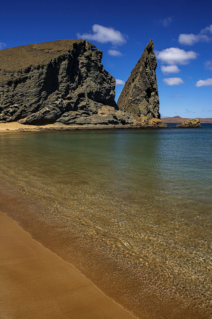 Friedlicher Strand mit ruhigem Wasser in der Nähe einer zerklüfteten Felsformation.