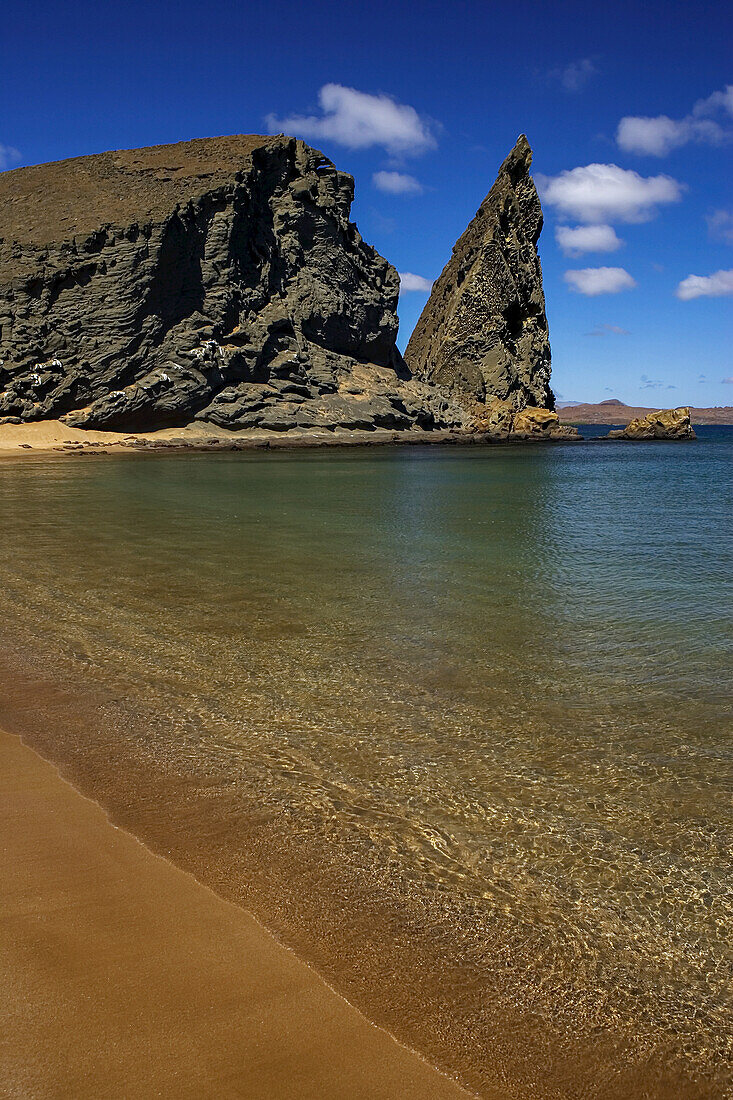 Peaceful beach with calm water near crumbled rock formation.