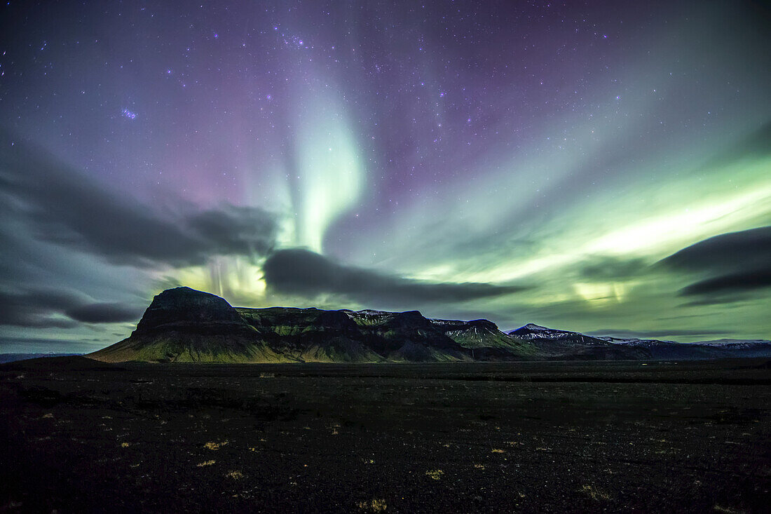 The northern lights dance over a mountain range on Iceland's South Coast; Vik, Southern Region, Iceland