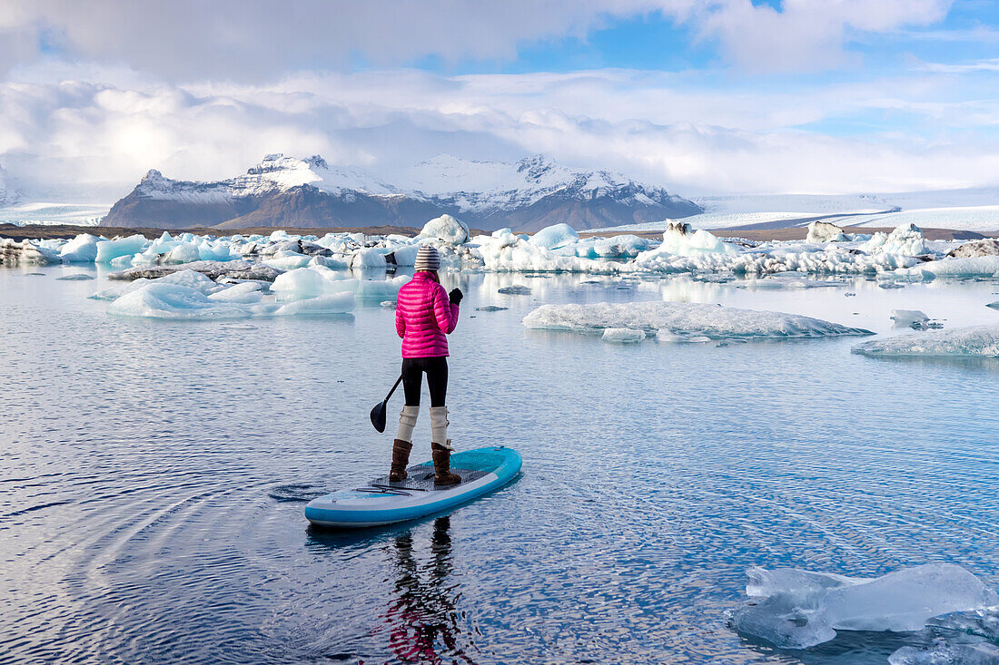 A woman on an inflatable paddleboard paddling on the Jokulsarlon glacier lagoon.