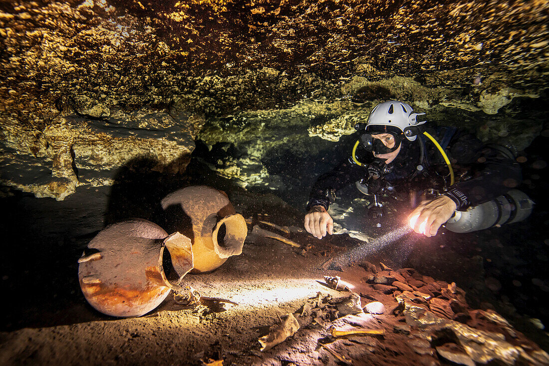 A cave diver examines ancient Mayan pots, a monkey skull, and human bones.