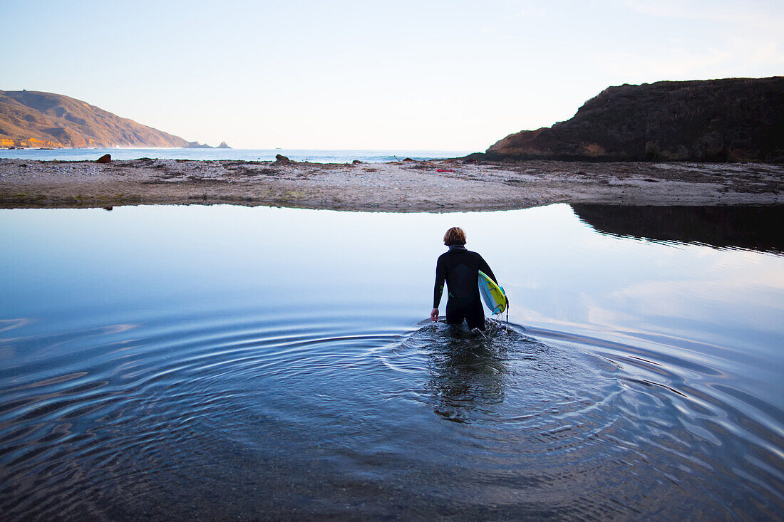 Ein Surfer überquert einen Bach, um zum Strand in Big Sur, Kalifornien, zu gelangen.