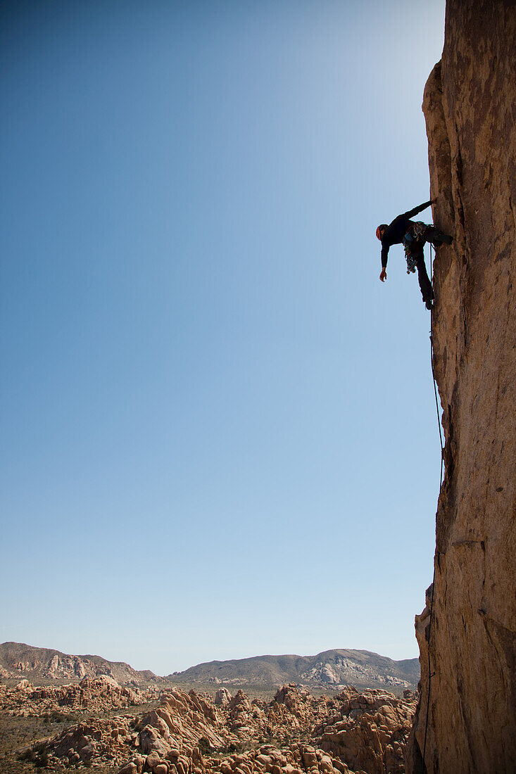 A trad Climber rests while climbing a vertical rock face.