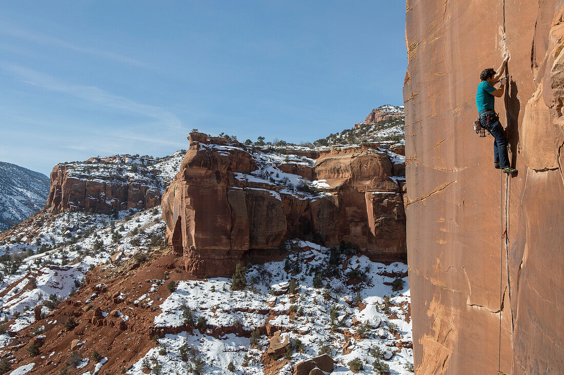 A man climbs sandstone cracks in Colorado desert.