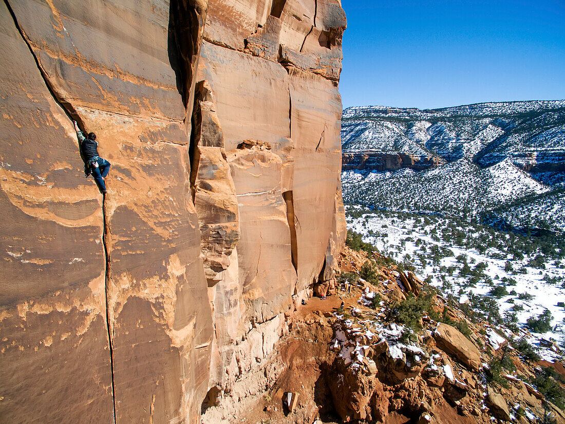 Ein Mann klettert in der Wüste von Colorado auf Sandsteinspalten.