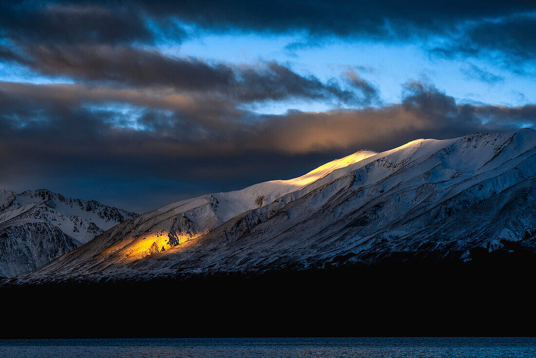 Das Licht des Sonnenuntergangs bricht durch die Wolken und erhellt einen Berg.