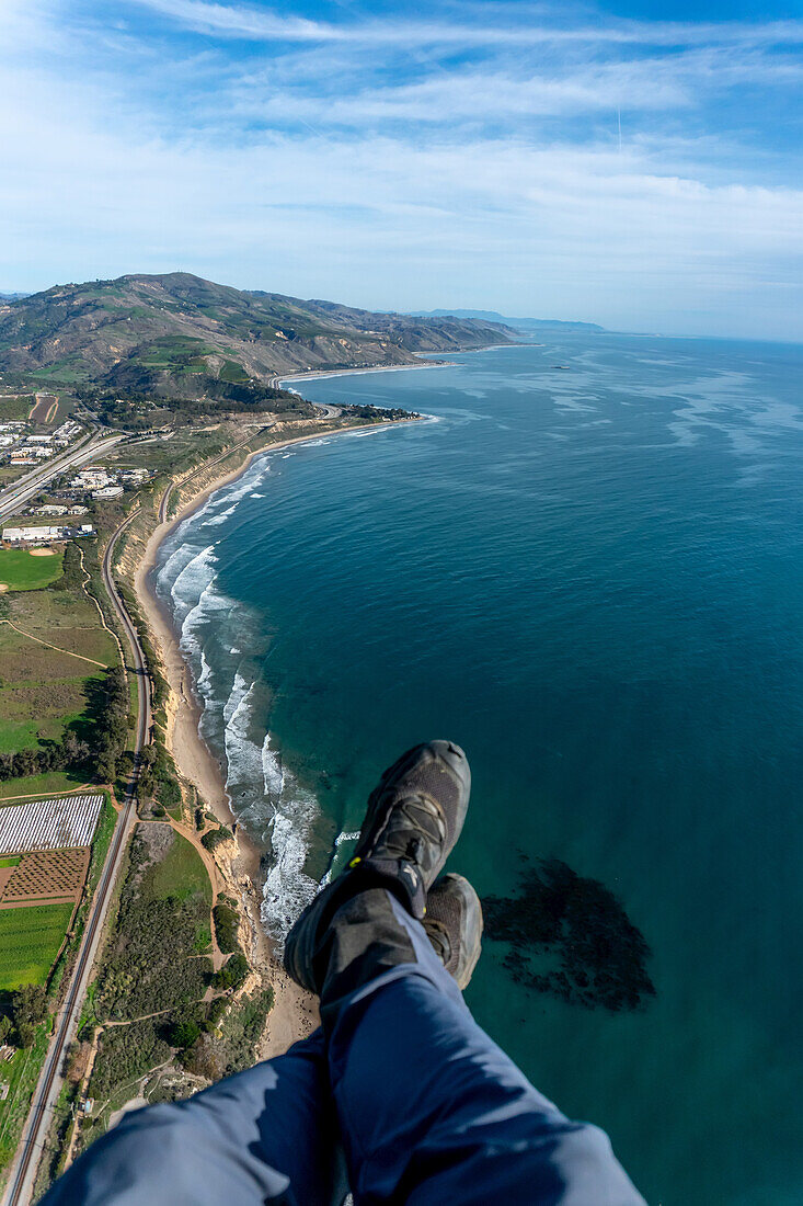Aerial view of a paramotorer with his feet dangling in the air high above the California coastline; Carpinteria, California, United States of America