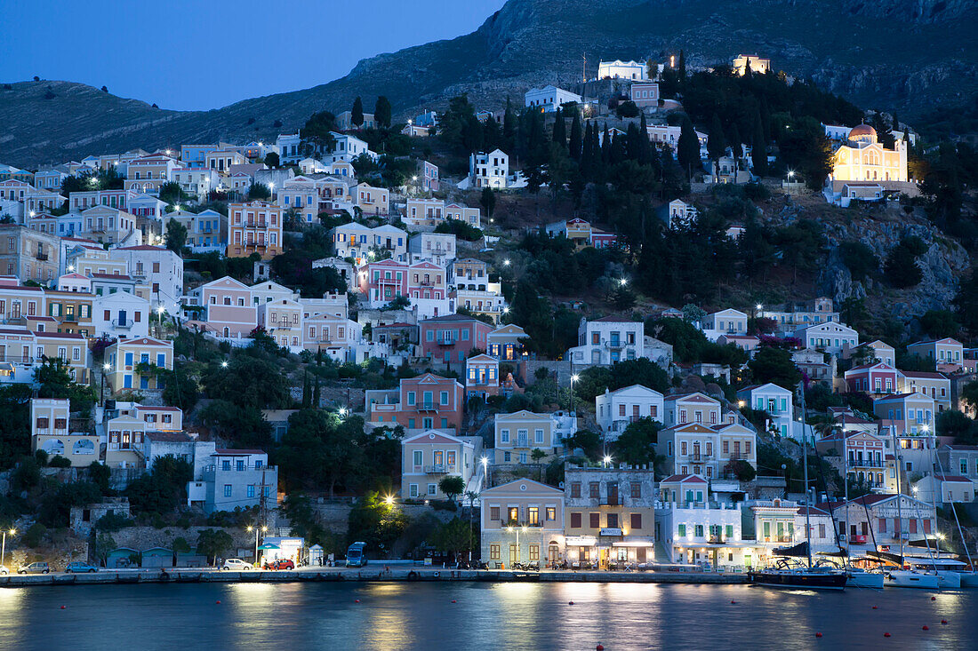 Illuminated buildings on the waterfront in the evening at Gialos Harbor, Symi (Simi) Island; Dodecanese Island Group, Greece