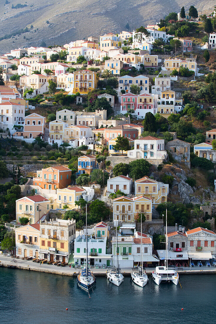 Overview of pastel colored buildings and sailboats moored along the seawall at Gialos Harbor, Symi (Simi) Island; Dodecanese Island Group, Greece