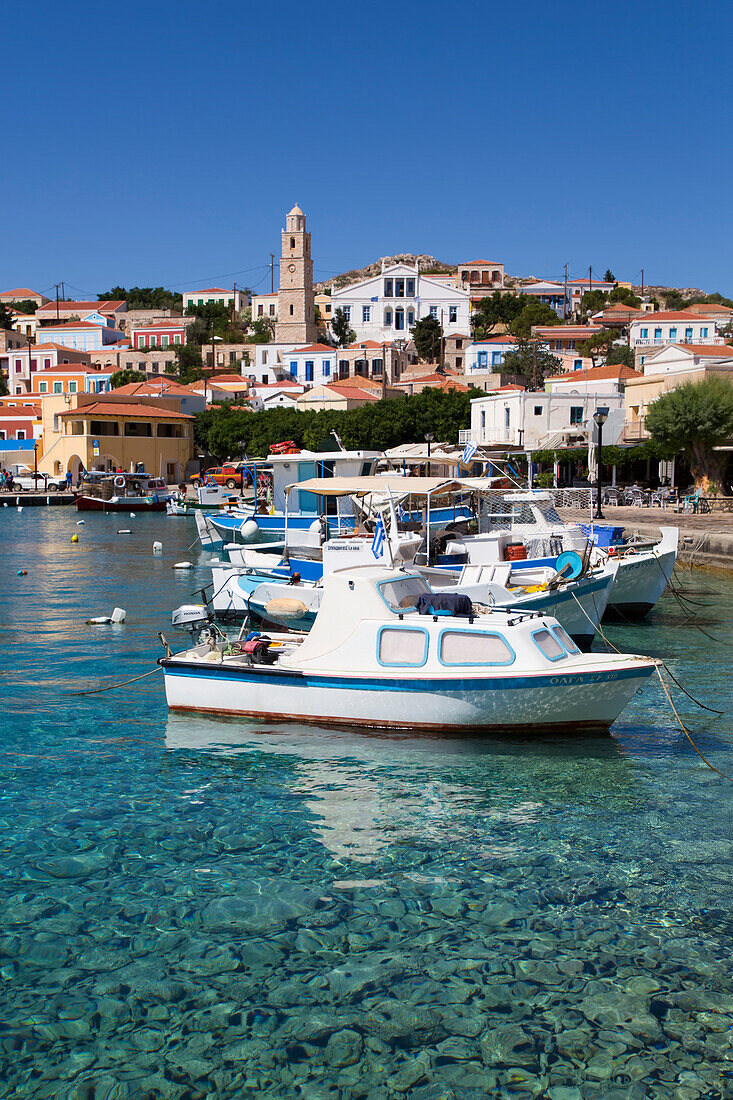 Close-up of fishing boats moored at the waterfront in Emborio Harbor with traditional buildings and the clock tower in the town center on Halki (Chalki) Island; Dodecanese Island Group, Greece