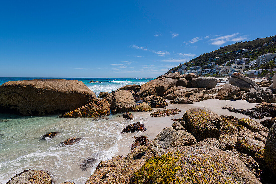 Large boulders along the rocky shore with beachfront buildings on the hillside at Clifton Beach; Cape Town, Western Cape, South Africa