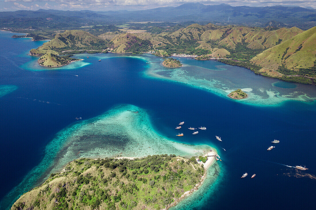 Luftaufnahme von Booten, die am Ufer einer Insel im Komodo-Nationalpark, der Heimat des berühmten Komodowarans, vertäut sind; Ost-Nusa Tenggara, Kleine Sunda-Inseln, Indonesien