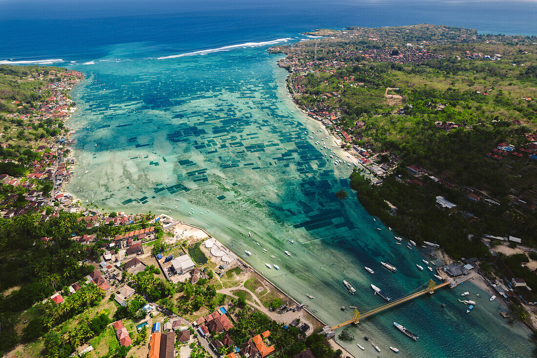 Luftaufnahme der Wasserstraße und der ikonischen Gelben Brücke, die Nusa Lembongan und Nusa Ceningan verbindet, auch mit den Unterwasserfeldern der Algenzucht unter dem seichten, türkisfarbenen Wasser; Klungkung Regency, Ost-Bali, Bali, Indonesien