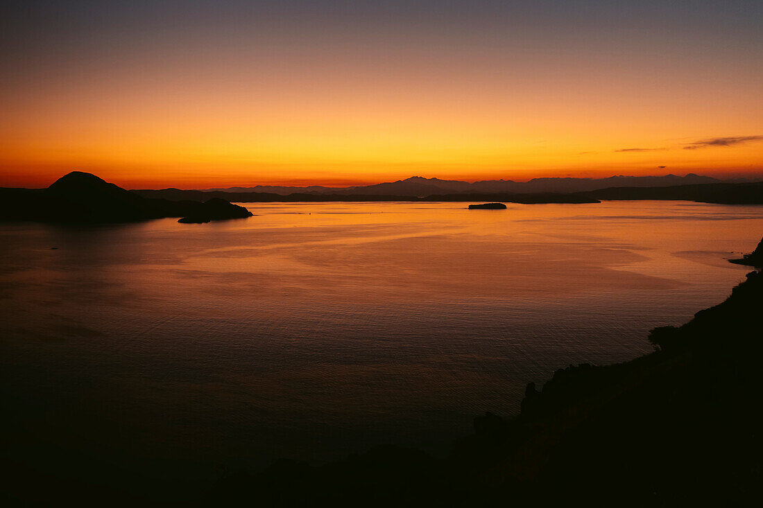 Bright yellow and orange glow of the sunset over the ocean and silhouetted islands in the Komodo National Park in the Komodo Archipelago; East Nusa Tenggara, Indonesia