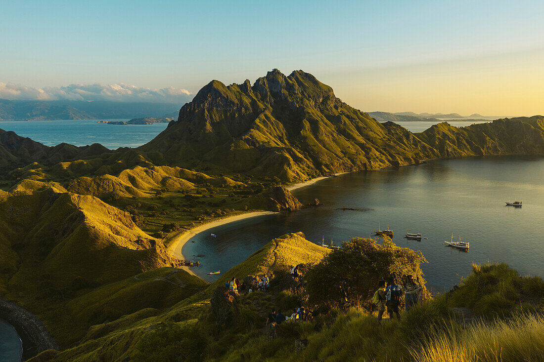 Reisende auf einem Hügel mit Booten in der Bucht der Insel Padar im Komodo Nationalpark im Komodo Archipel; Ost Nusa Tenggara, Indonesien